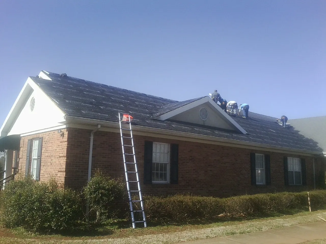 Crew tearing shingles off a brick ranch roof with a ladder set — Emergency Roof Repair work by our crew in Grampian