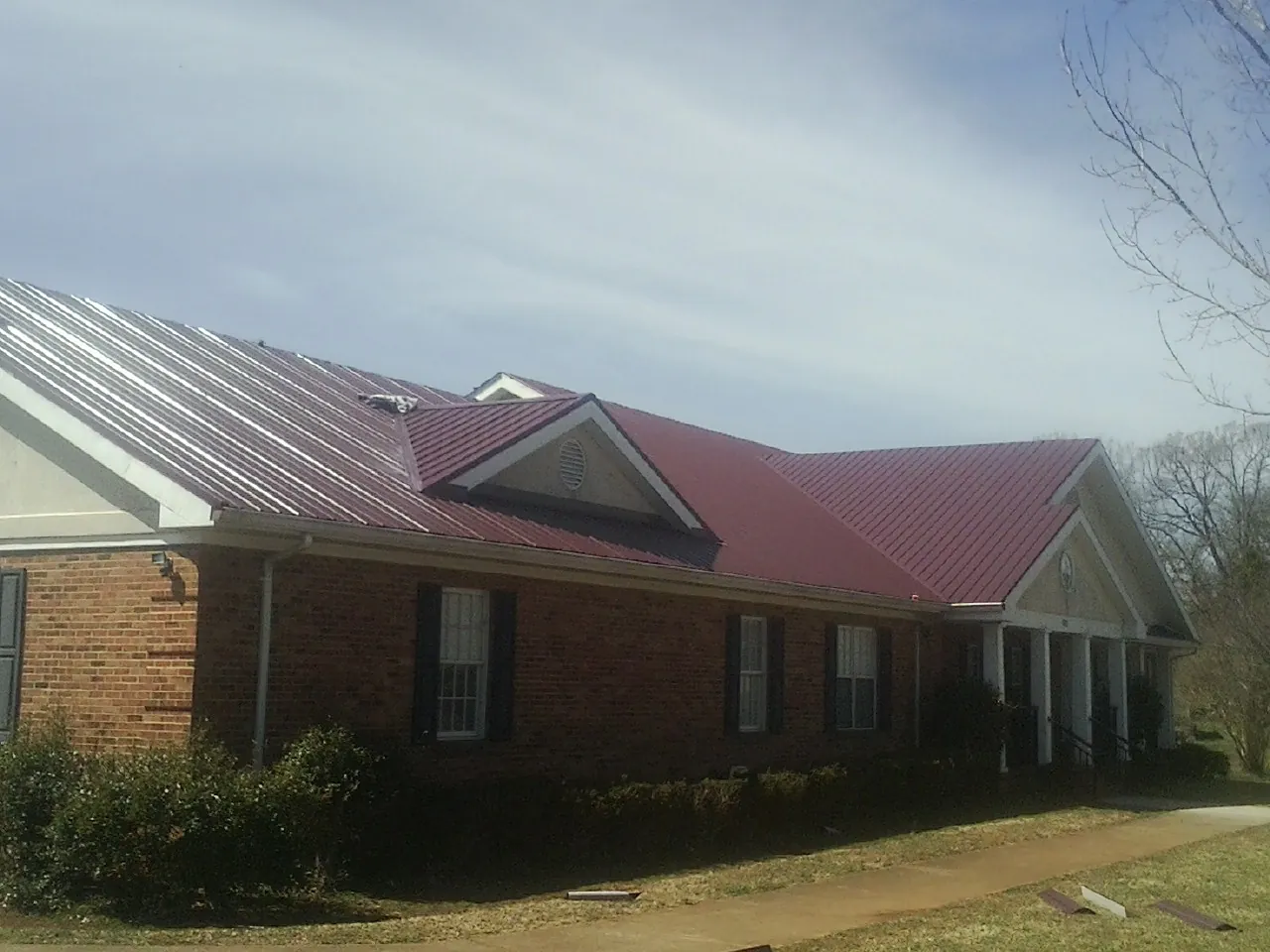 Red metal roof with gabled entries on a long brick building, from a Hail Damage Roof Repair job in Grampian