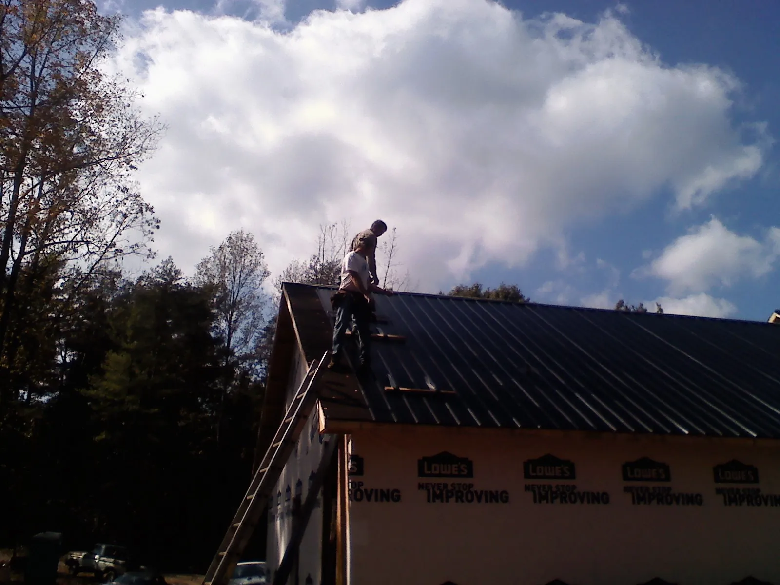 Roofer fastening dark metal panels high against a cloudy sky, from a Roof Inspection job in Grampian