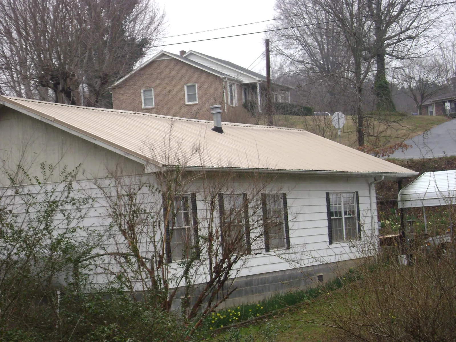 Tan metal roof on a white sided house set into a hillside — Commercial Roofing by Roofing Brothers in Grampian