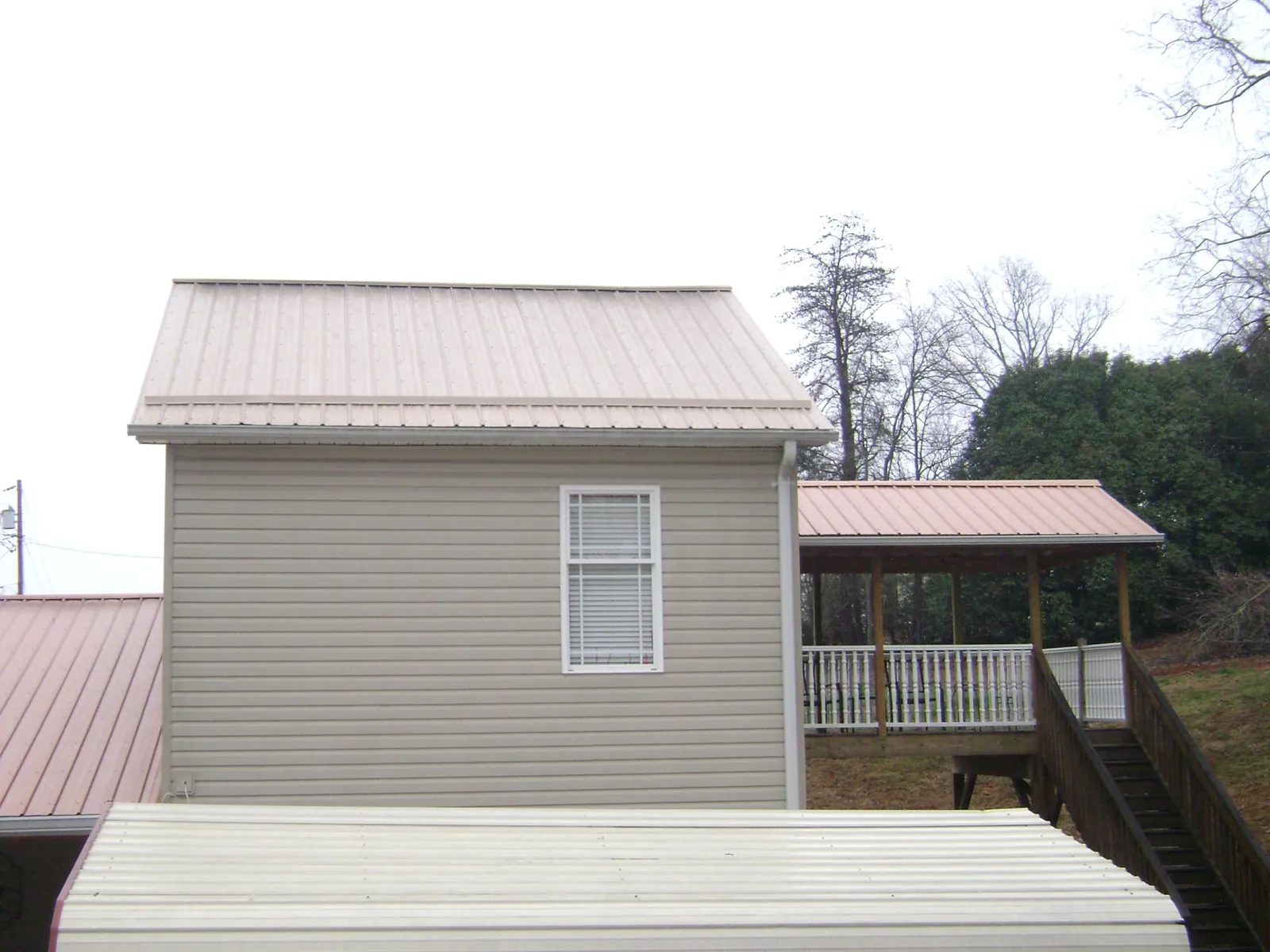 Tan metal roofs on a two story addition and attached porch, from a Roof Replacement job in Grampian